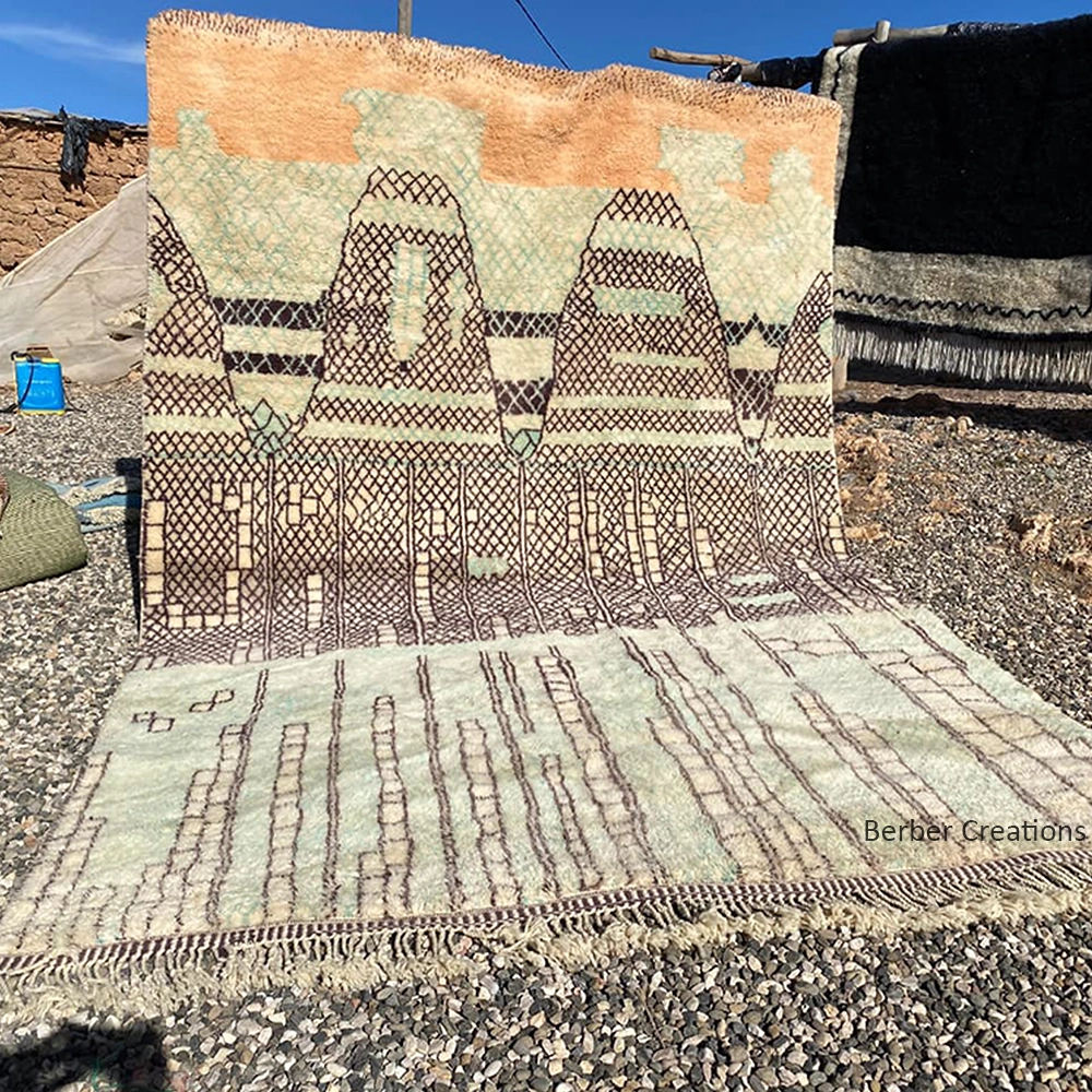 Hand-knotted Moroccan Berber wool rug featuring an abstract mountain landscape design with sunset orange peaks and mint green geometric patterns.