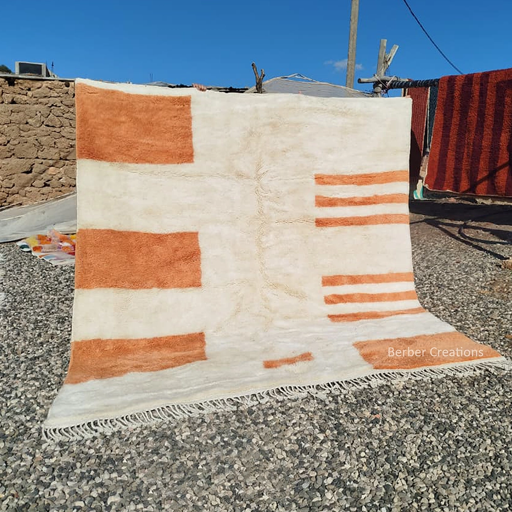 Hand-knotted minimalist ivory Moroccan Berber wool rug featuring asymmetrical apricot orange geometric blocks, horizontal stripes, and a plush cream pile with ivory tassels