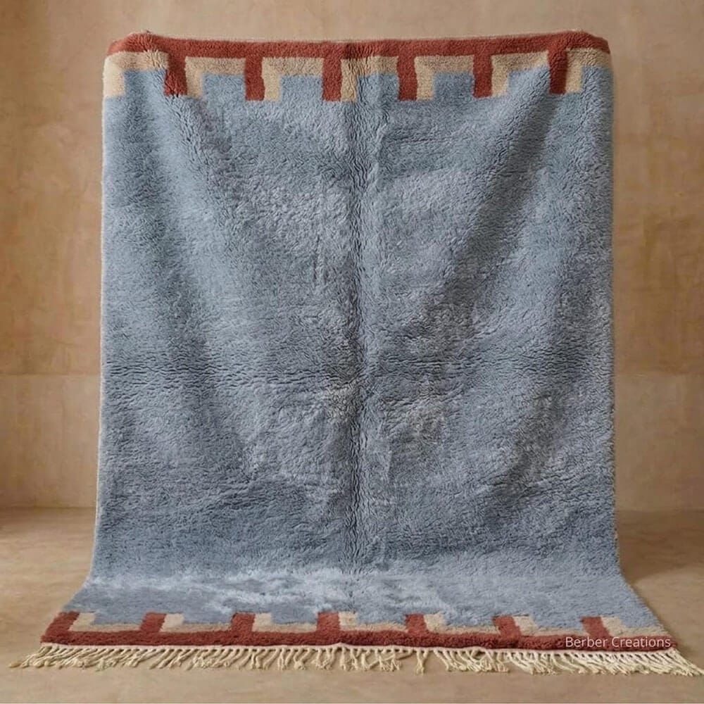 Anir handmade Moroccan Berber wool rug featuring a plush slate blue field framed by terracotta and beige crenellated castle-like border details with tassel fringe.
