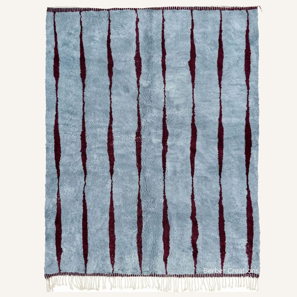 Asklu handmade Moroccan Berber wool rug featuring a plush dusty blue pile structured by organic burgundy vertical stripes with braided natural fringe.