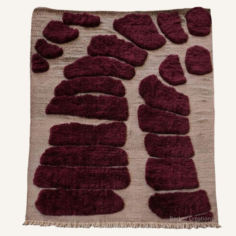 Ifri Stone handmade Moroccan Berber wool rug featuring raised deep burgundy organic stone-like shapes arranged in a stepping-stone formation on a neutral oatmeal beige woven field with braided tassel fringe.