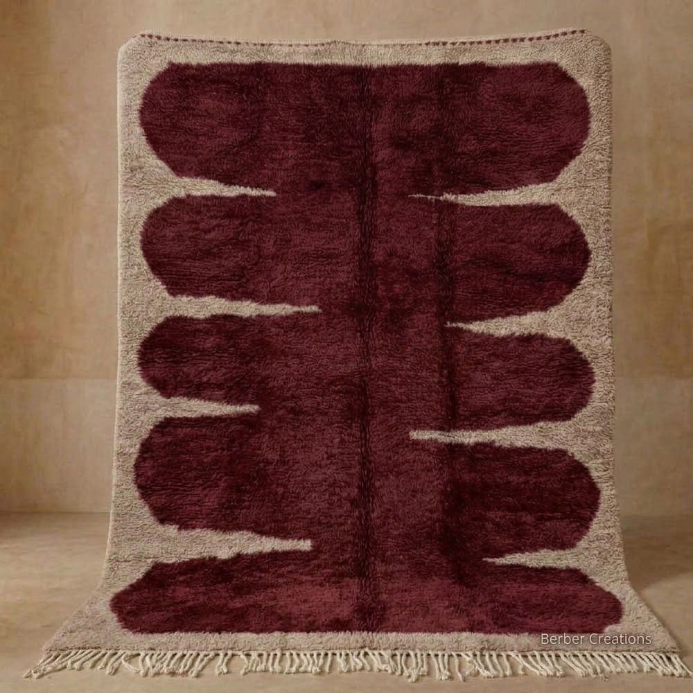 Tazoughart Wave handmade Moroccan Berber wool rug featuring a bold deep burgundy organic wave central motif on a natural beige field with braided fringe.