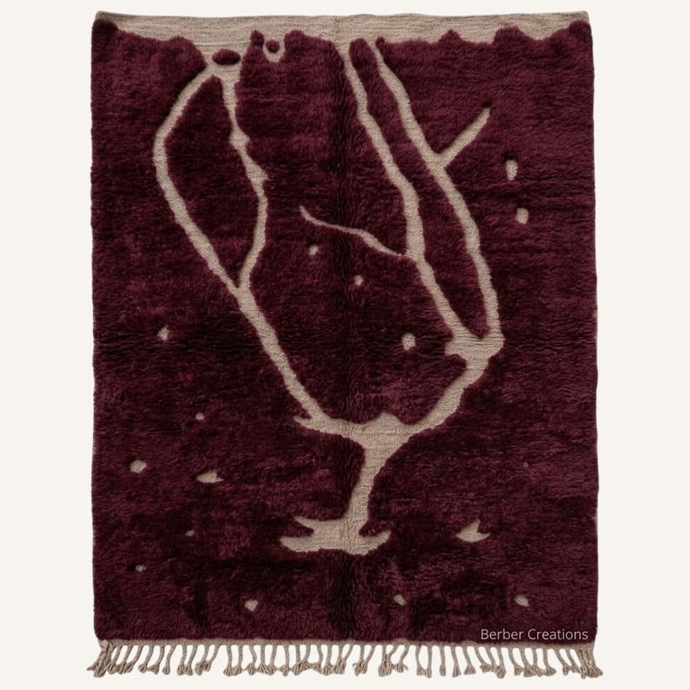 Delya handmade Moroccan Berber wool rug featuring a deep plush burgundy field woven with a large fluid sand-colored abstract outline motif, scattered dot accents,