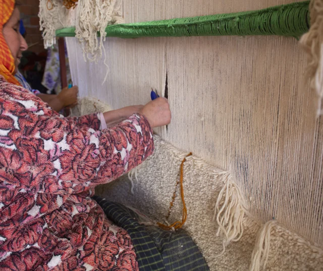 Master weaver at Berber Creations workshop in the Atlas Mountains hand-knotting a traditional Beni Ourain rug